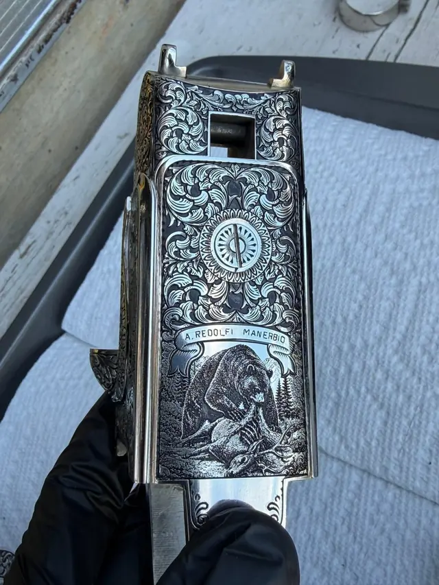 Engraved shotgun receiver with a bear and deer scene and floral scroll border